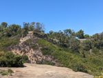 Sun-drenched view across the canyon. Bare rock cliffs with shady holes in them. Eucalyptus trees along the far ridge.
