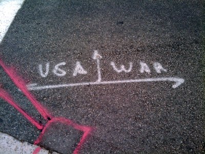 Spray-painted markings on street: USA, WAR and arrows.