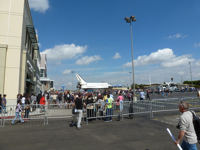 Parking lot with temporary fences, lots of people, and a space shuttle in the distance.