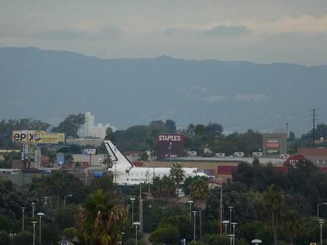 Space Shuttle in a STAPLES parking lot, seen from a ways off.
