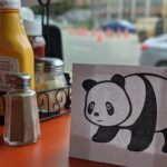 Panda on a lunch table next to salt, pepper, mustard etc.