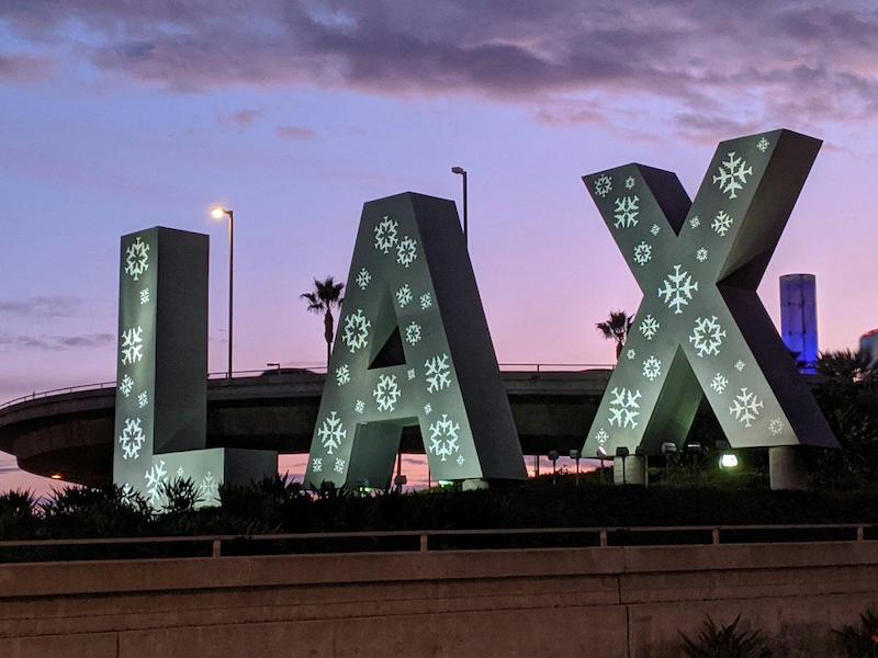 Giant free-standing LAX letters with snowflake decorations on them, against a purple twilight sky.