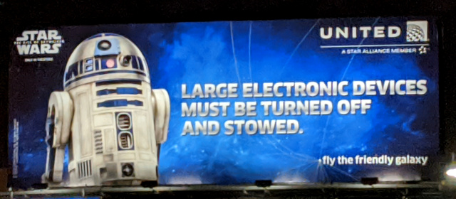 Sign with R2-D2 and the text: Large electronic devices must be turned off and stowed.