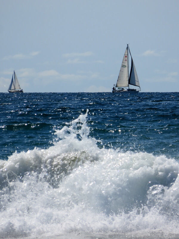 Sailboats in the distance, ocean spray in the foreground.