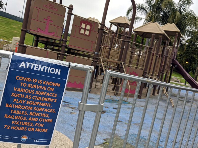 Empty playground with a temporary fence and a sign reminding you just how long the coronavirus can last on surfaces like, well, playground equipment.