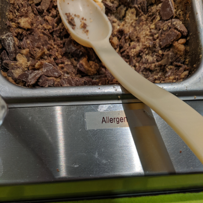 Bin full of Butterfinger crumbles and a spoon, labeled just Allergens.