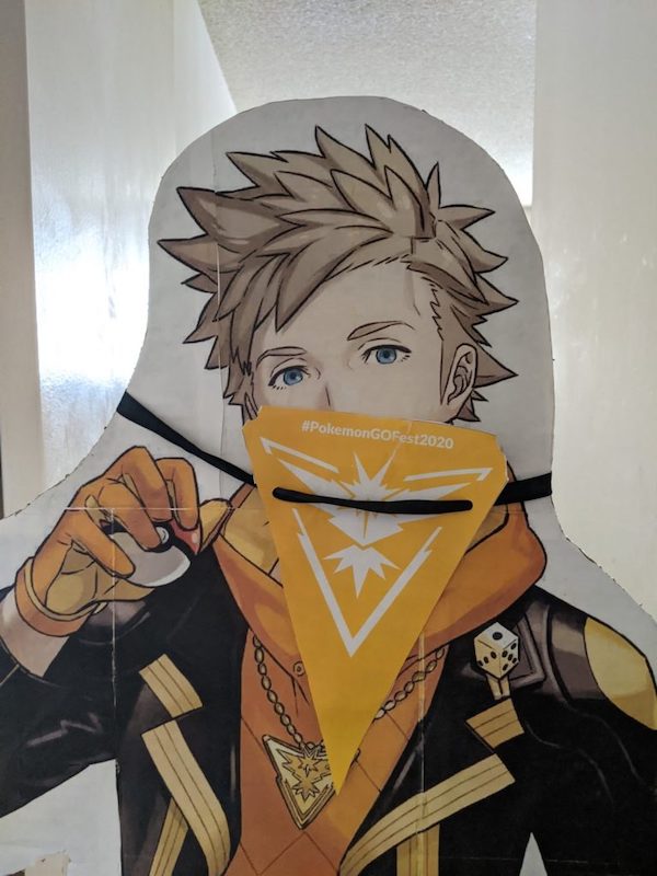 ead and shoulders of a cardboard cutout of Spark (Pokemon Go) with a pennant covering his mouth and nose like a bandana.