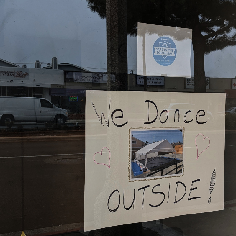 A sign on a window for a dance class studio that says We Dance Outside with a picture of an awning set up in the parking lot.