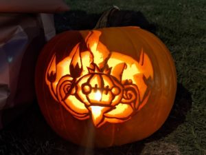 A pumpkin carved with an image of a Chandelure, a chandelier-like Pokemon, lit from inside.