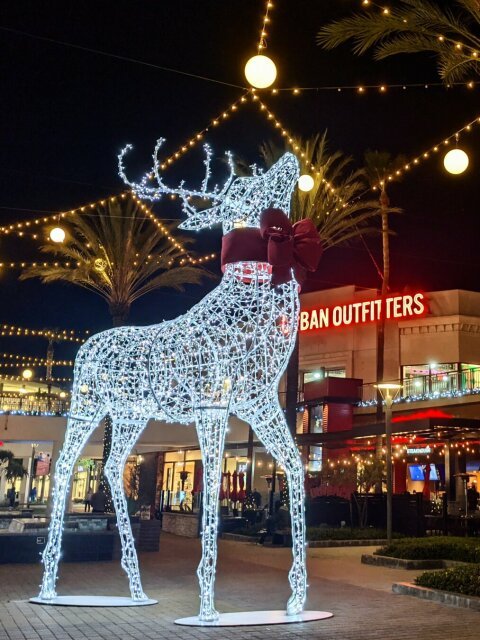 A giant wire reindeer in an open shopping area, lit up brightly at night. In the background, BAN OUTFITTERS can be seen.